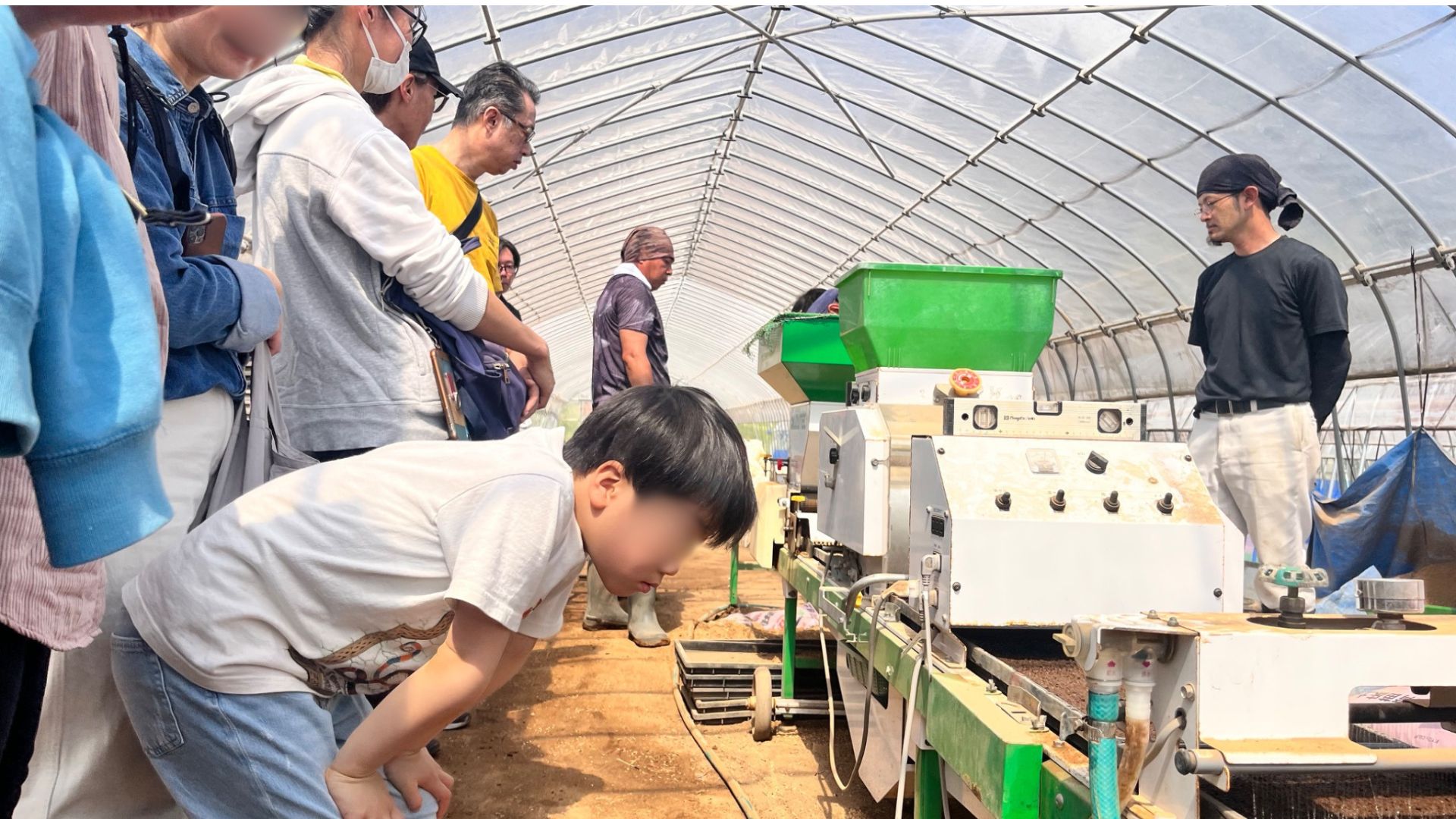 ビニールハウスの中で種まき機を見学する子どもと参加者
