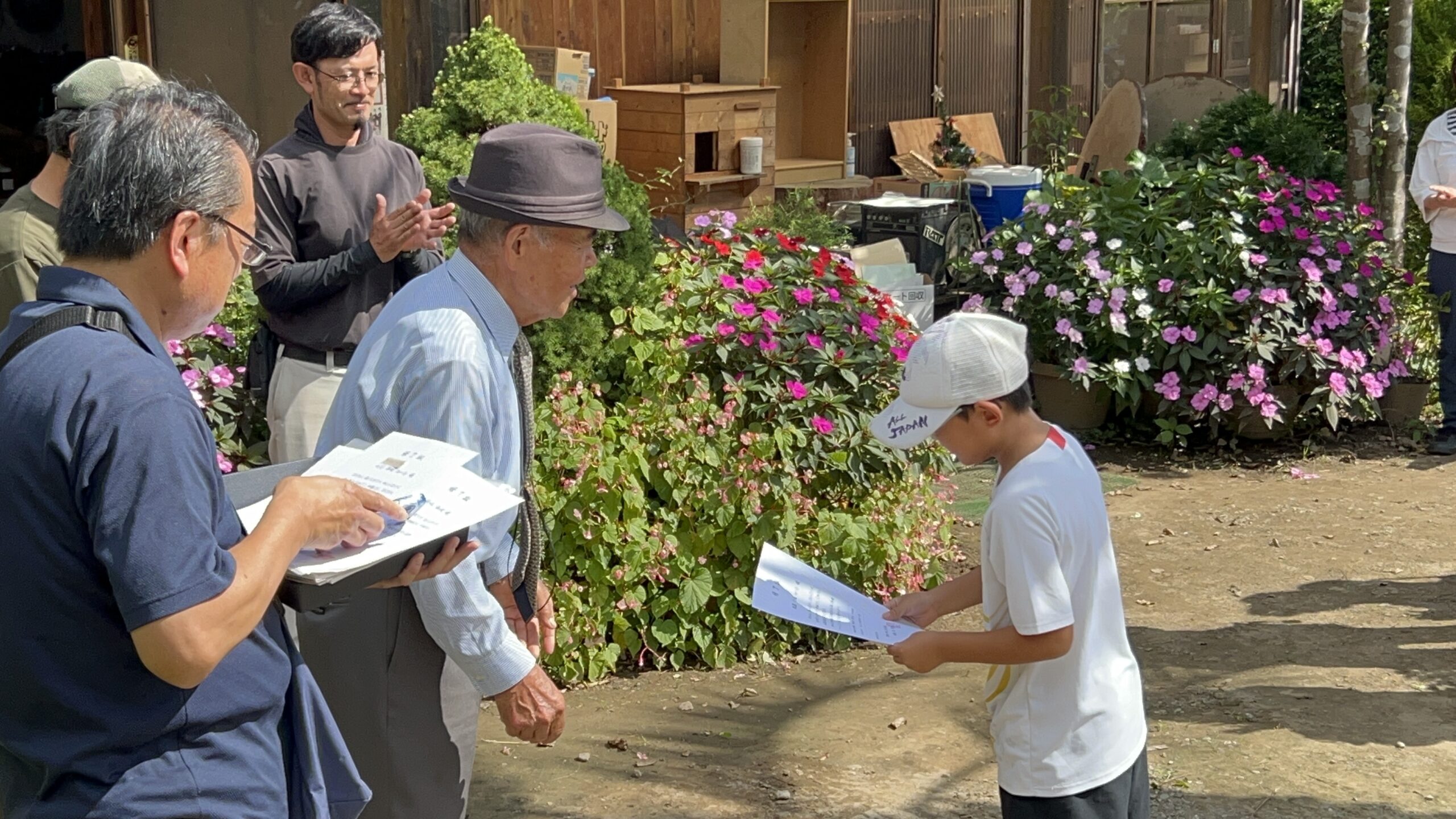 終了式で証書を手にする子どもと拍手を送る大人たち